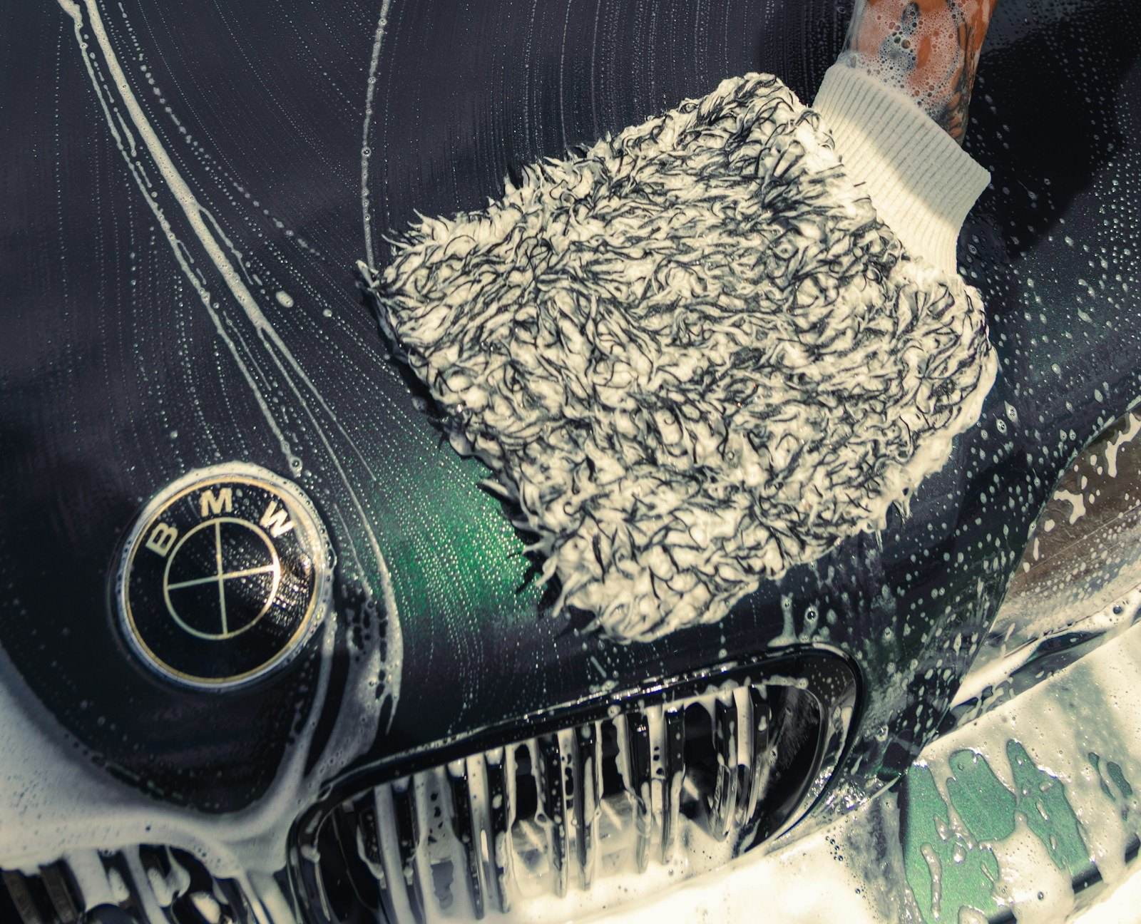 Guante de microfibra lavando a mano el capó oscuro de un carro con espuma
