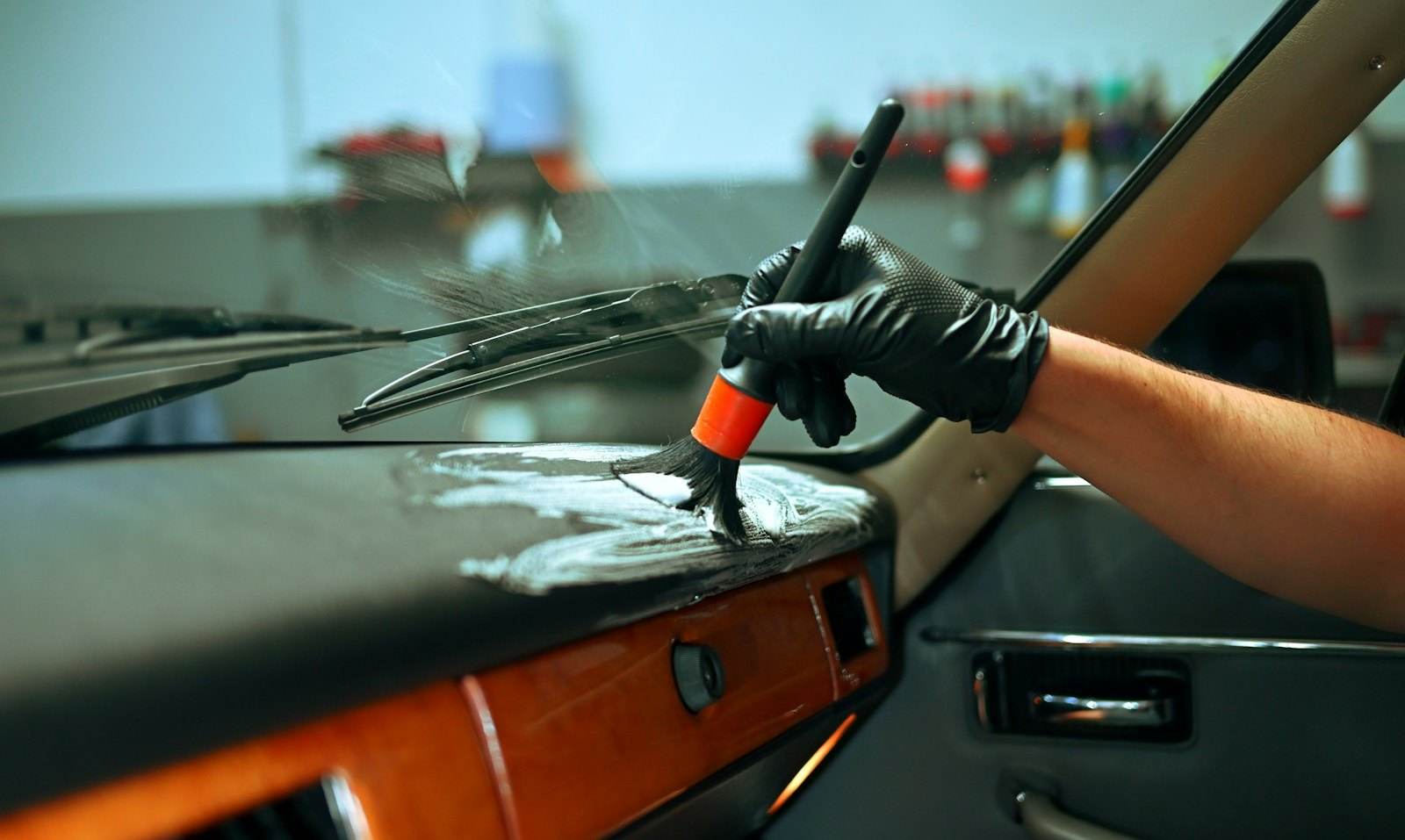 Mano con guante limpiando a fondo el dashboard de un vehículo con un cepillo de detailing